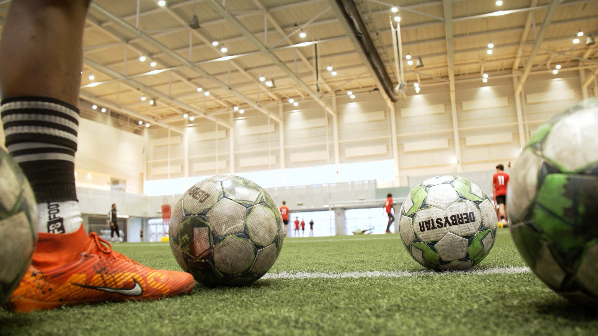 Soccer player's foot at field level with several soccer balls